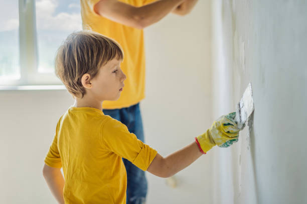 man with his son makes repairs at home, he teaches children to plaster the walls with a spatula in his hands - plaster plasterer work tool child foto e immagini stock