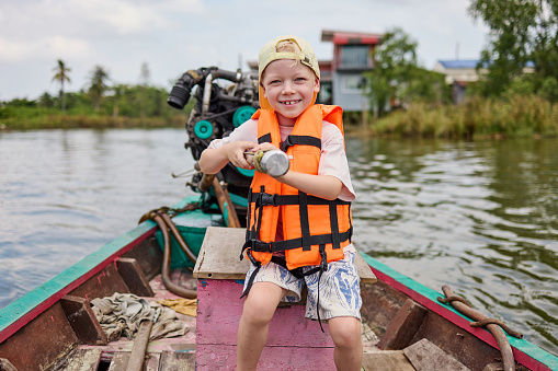 A young boy steers a longtail boat during an excursion on a canal in Thailand