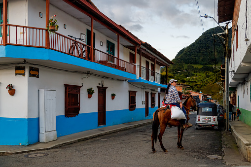 Jardin, Colombia - January 12, 2023: Coffee farmer woman riding a horse visits the town at sunset