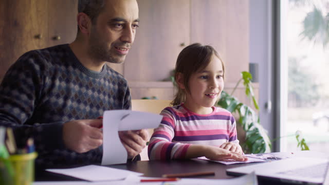 Father and daughter making their own toys of paper following steps instructed in the video tutorial on laptop computer