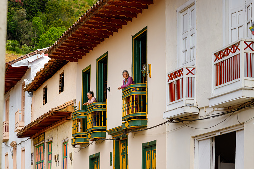 Jerico, Colombia - January 14, 2023: Two older women look out of the balconies of their colorful houses