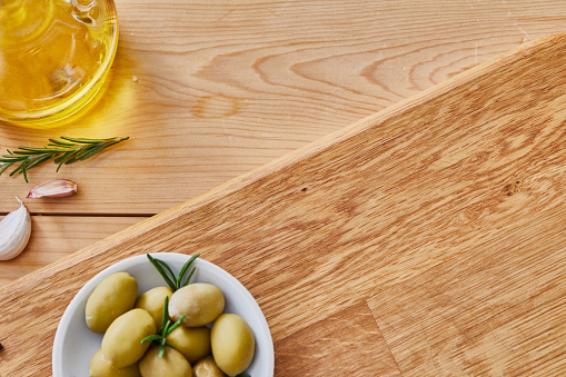 A view of fresh olives in a handmade ceramic bowl on the kitchen table, with garlic and rosemary on a wooden cutting board, an image with a copy space