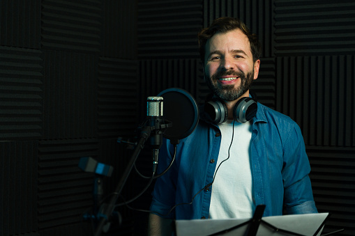 Cheerful man with headphones recording audio in a professional sound booth