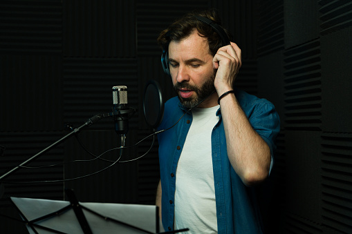 A focused man recording voice-over with headphones in a soundproof studio