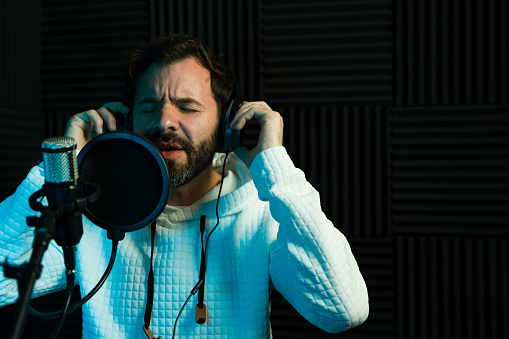 Male singer with headphones performing in soundproof recording studio, artistic expression