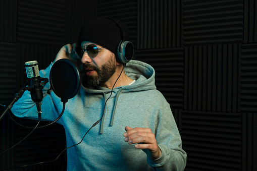Male singer with a beanie and headphones recording a new song in a studio