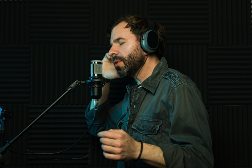 Focused man singing into a microphone while wearing headphones in a soundproof studio