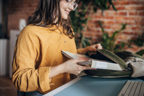 Beautiful young woman putting books in backpack at home.