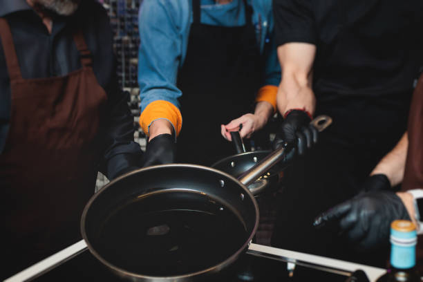 Group of guests in a cooking class studio, adults preparing different dishes in the kitchen together, people in aprons learn on culinary master class, chef uniform, hands in gloves, italian cuisine