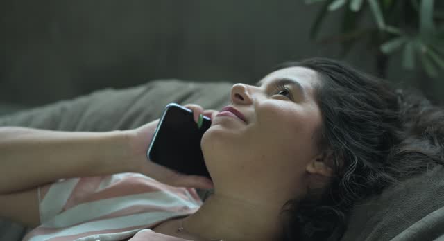 Young woman lying down, smiling while talking on the phone