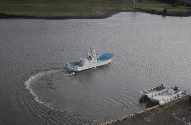 Abashiri, Japan - June 1, 2023: A commercial boat leaves the dock at Abashiri River on an early morning. Background shows a riverside park on the north shore. Spring in the Okhotsk Subprefecture.