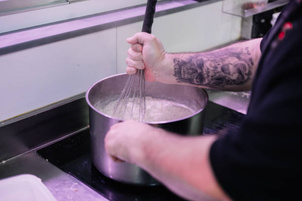 closeup of a chef's hands whisking the contents of a pot in his kitchen, showcasing the food preparation process and attention to detail in the kitchen