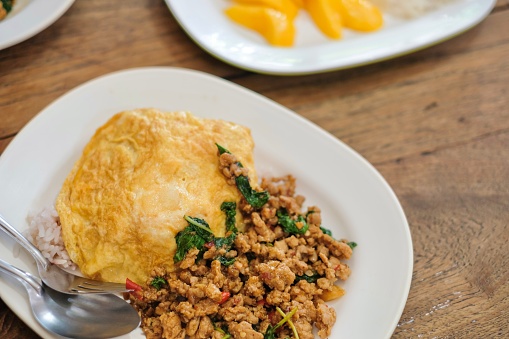 A plate of pad kra pao (holy basil pork mince stir-fry) with omelette and mixed grain rice, and a dessert of fresh mango slices with sticky rice at a street food stall in Phra Nakhon, near the Grand Palace - Bangkok, Thailand