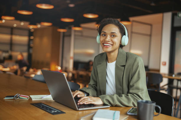 istock A woman in formal wear is seated at a table, smiling, using a laptop computer in nice modern coworking office 2082146648