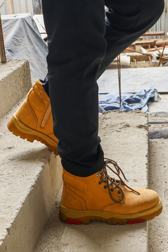 Photo of a man walking wearing light brown leather safety shoes in a building construction