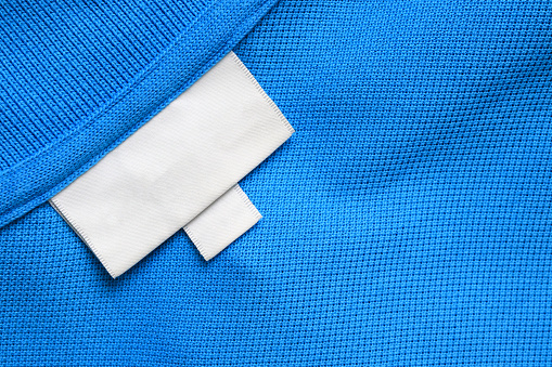 Blank white laundry care clothes label on blue shirt fabric texture background