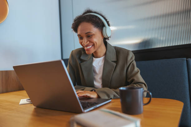 istock Woman with headphones at desk using laptop, smiling 2082181218