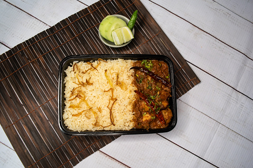 Achari chicken pulao biryani rice with cucumber and lemon slice served in dish isolated on wooden table side view of bangladeshi and indian spicy lunch food