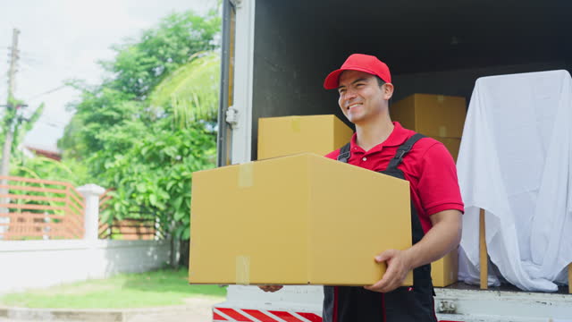Side view portrait of delivery man stand with hold the box and look forward with smiling stay in the back on truck.