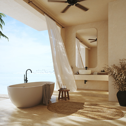 Luxurious bathroom located on a tropical island.
Designed to blend seamlessly with the serene beachfront, it features a freestanding bathtub, sandy hues, and natural textures. 
The gentle breeze flutters through white curtains, while the panoramic view of the azure sea invites a sense of calm and relaxation.