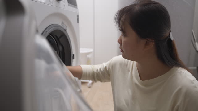 Asian woman loading washing machine putting dirty clothes