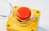 Close-up shot of a red emergency stop button with a protective clear casing mounted on a yellow panel, safety mechanism for heavy industrial equipment shutdown, workers safety rules, policies concept