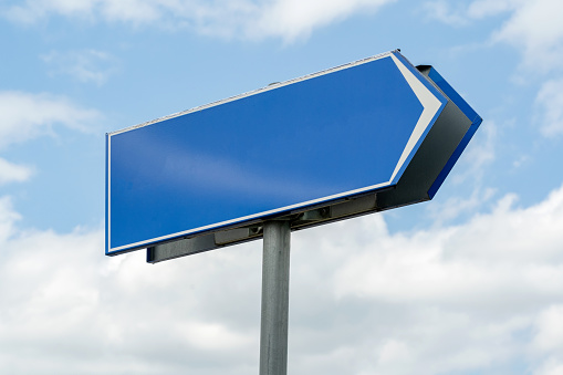 Empty blue highway sign with a directional arrow pointing right, set against a daytime sky with scattered clouds, route direction signage, advertising, right turn abstract concept, progress, nobody