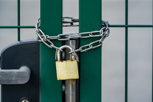 Green gate secured with a strong chain and a generic padlock, object closeup. Security and safety of premises, locked out lot, closed apartment complex or enclosed area abstract concept, nobody