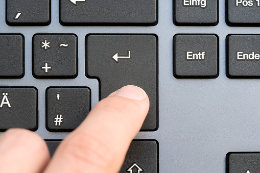 Finger captured in the moment of pressing the Enter key on a sleek modern design keyboard, submission of data, sending a message, chatting, adding to cart simple abstract concept, one person, top view