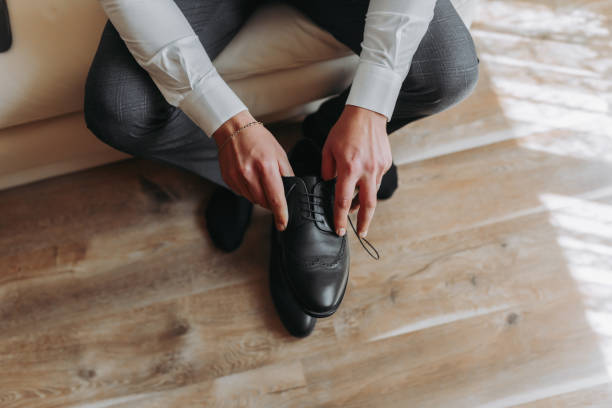 homme en costume, marié, gros plan mettre des chaussures, tenant des chaussures noires, attacher des lacets - suit necktie close up gray photos et images de collection