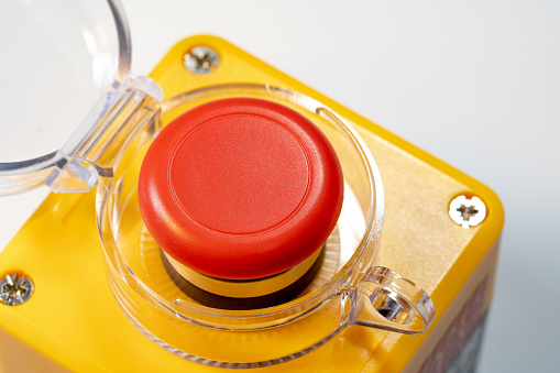 Detailed closeup view of a red emergency stop button industrial machine safety off switch, red yellow panic button with cover open lifted. Heavy duty equipment, workplace safety, worker security