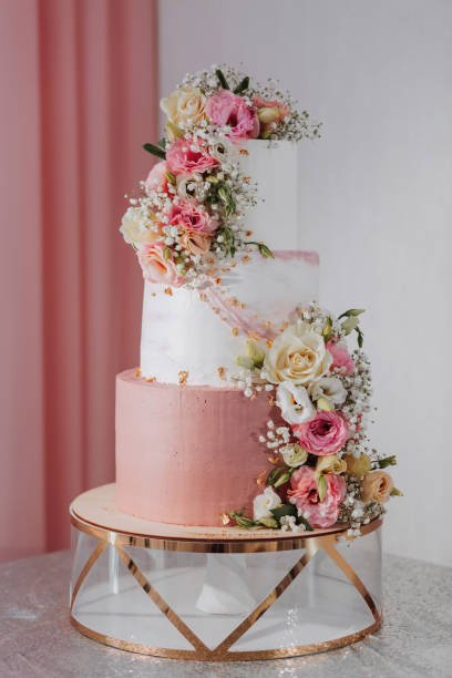 istock Three-tiered white wedding cake decorated with various flowers on silver surface and pink background in wedding hall. 2082306845