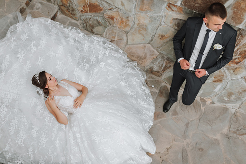 a young beautiful bride with blue eyes in a wedding dress, lying on stone steps, her husband is next to her. The photo is taken from above