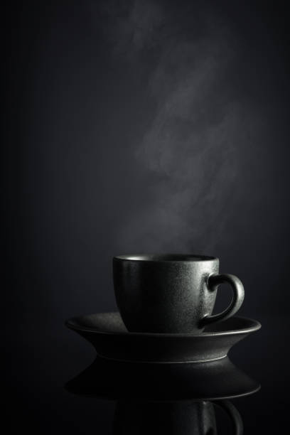 Black cup of coffee on a black reflective background.
