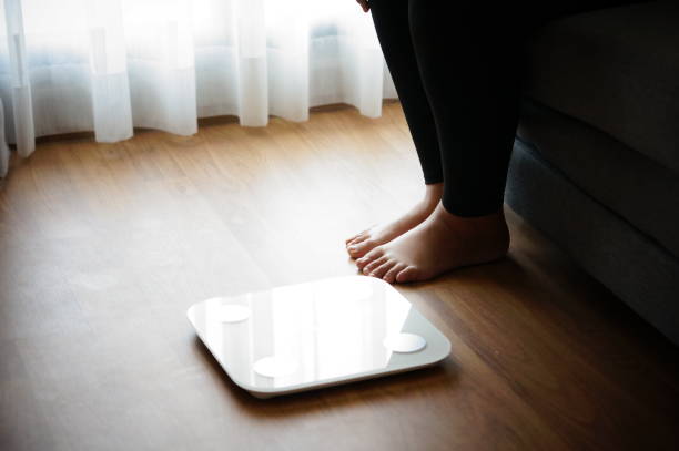 istock Fat diet and scale feet standing on electronic scales for weight control. Measurement instrument in kilogram for a diet control. 2082383145