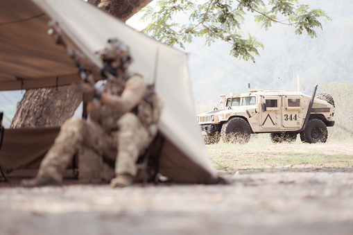 A military man or airsoft player in a camouflage suit sneaking the rope bridge and aims from a sniper rifle to the side or to target.