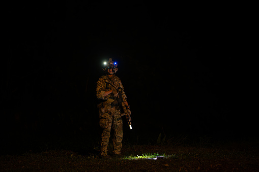Soldiers in camouflage uniforms hold weapons with patrol missions at night