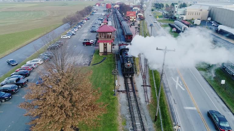 Aerial View of a Train Station, with a Steam Passenger Train, Pulling into the Station, Blowing Smoke, in Slow Motion on a Partially Sunny Day