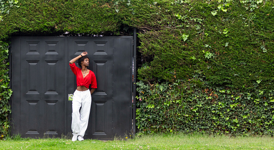 Young woman with afro hairstyle posing next to a black door in a lush green park