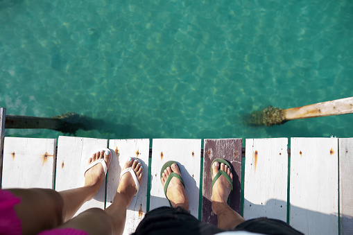 Summer travel concept Feet on a wooden bridge by the sea and clear waters