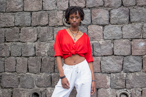 Young afro woman posing on stone wall background wearing red and white clothes in daylight