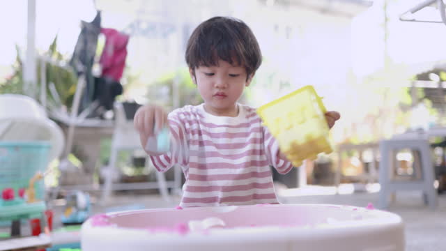Happy Asian boy play with pink science sand on the toy tray at home. Makes more focused.