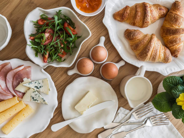 Delicious varied breakfast, brunch - croissants, eggs, ham, cheese, butter, apricot jam, fresh vegetable salad on a wooden table, top view