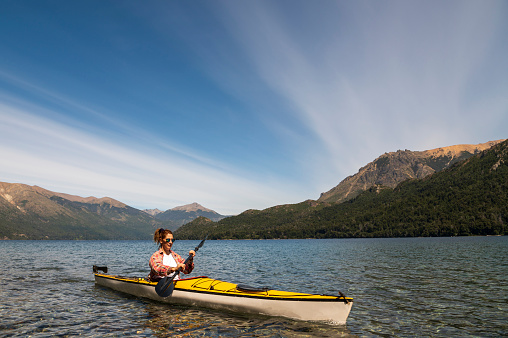 Beautiful woman enjoying summer vacation with her yellow tourist kayak in the southern Argentine lakes, Nahuel Huapi National Park in the city of San Carlos de Bariloche, Argentina.