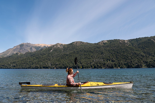 Young man enjoying summer vacation with his yellow tourist kayak in the southern Argentine lakes, Nahuel Huapi National Park in the city of San Carlos de Bariloche, Argentina.