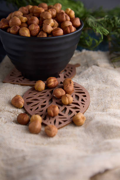 Very delicious nut, nutritious hazelnuts in a black cup on old burlap and a coniferous branch. Plate of hazelnuts stands on a figured wooden stand in the shape of a leaf on burlap.