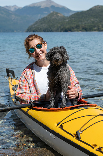 Beautiful woman paddles a kayak with her best company, her dog who sits on top of her. Together they enjoy summer vacations in San Carlos de Bariloche, Patagonia, Argentina.