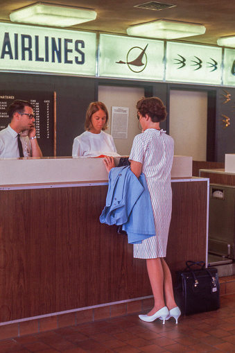 Madison, Wisconsin, USA - August 1967: Woman checking in for her flight at the North Central Airlines desk. Her bag is checked and she is receiving her paper boarding pass.