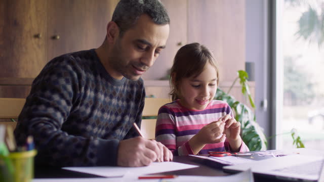 Father and daughter making their own toys of paper following steps instructed in the video tutorial on laptop computer