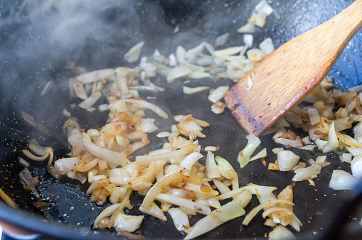 Culinary preparation: Chopped onion simmering with wooden utensil.